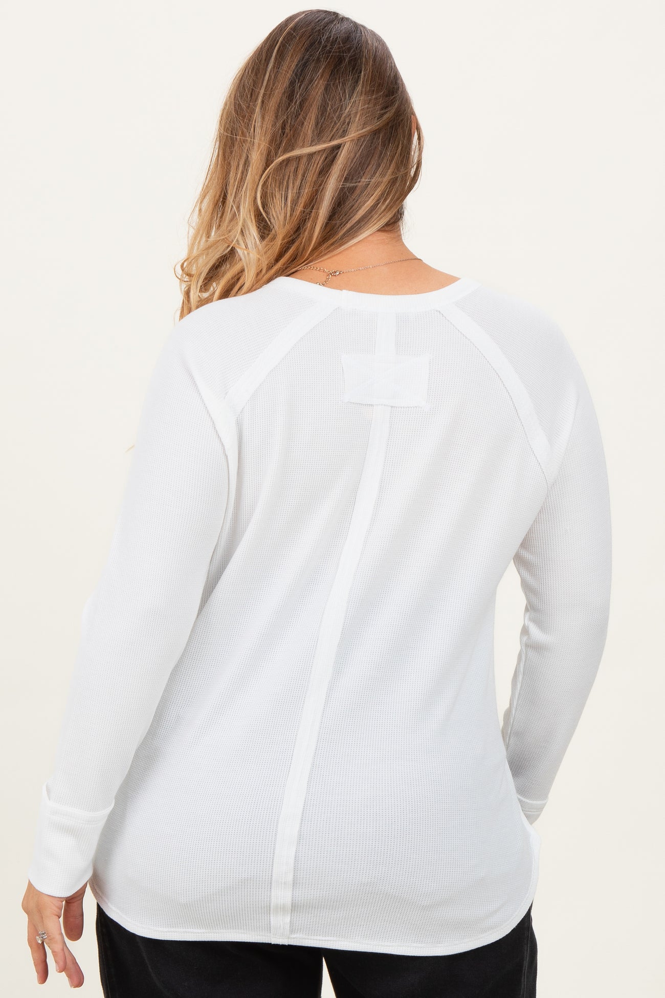 woman wearing a white long sleeve maternity top with a back seam detail and relaxed fit