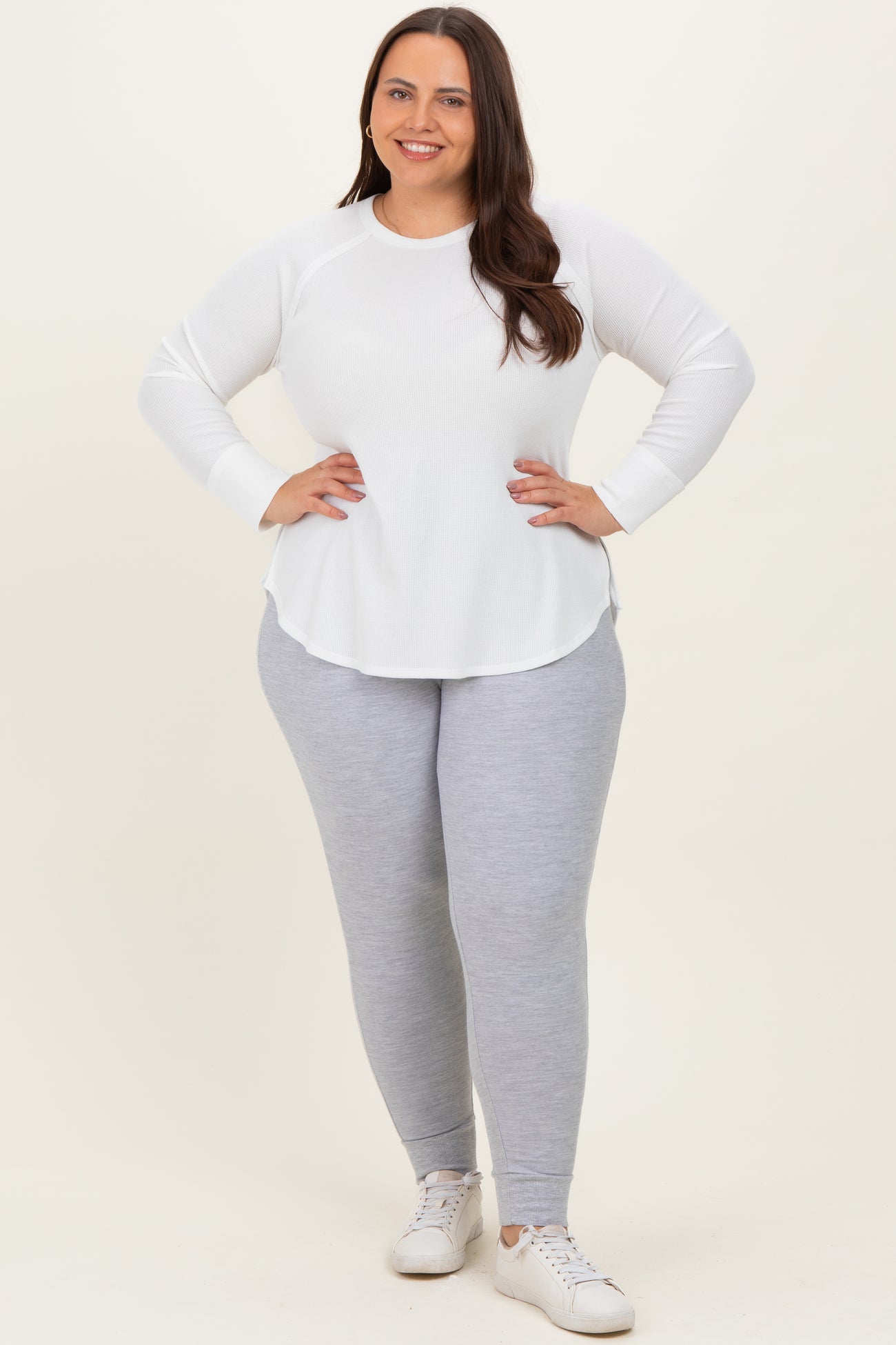 woman wearing a white long sleeve waffle knit top and light grey leggings, standing with hands on hips