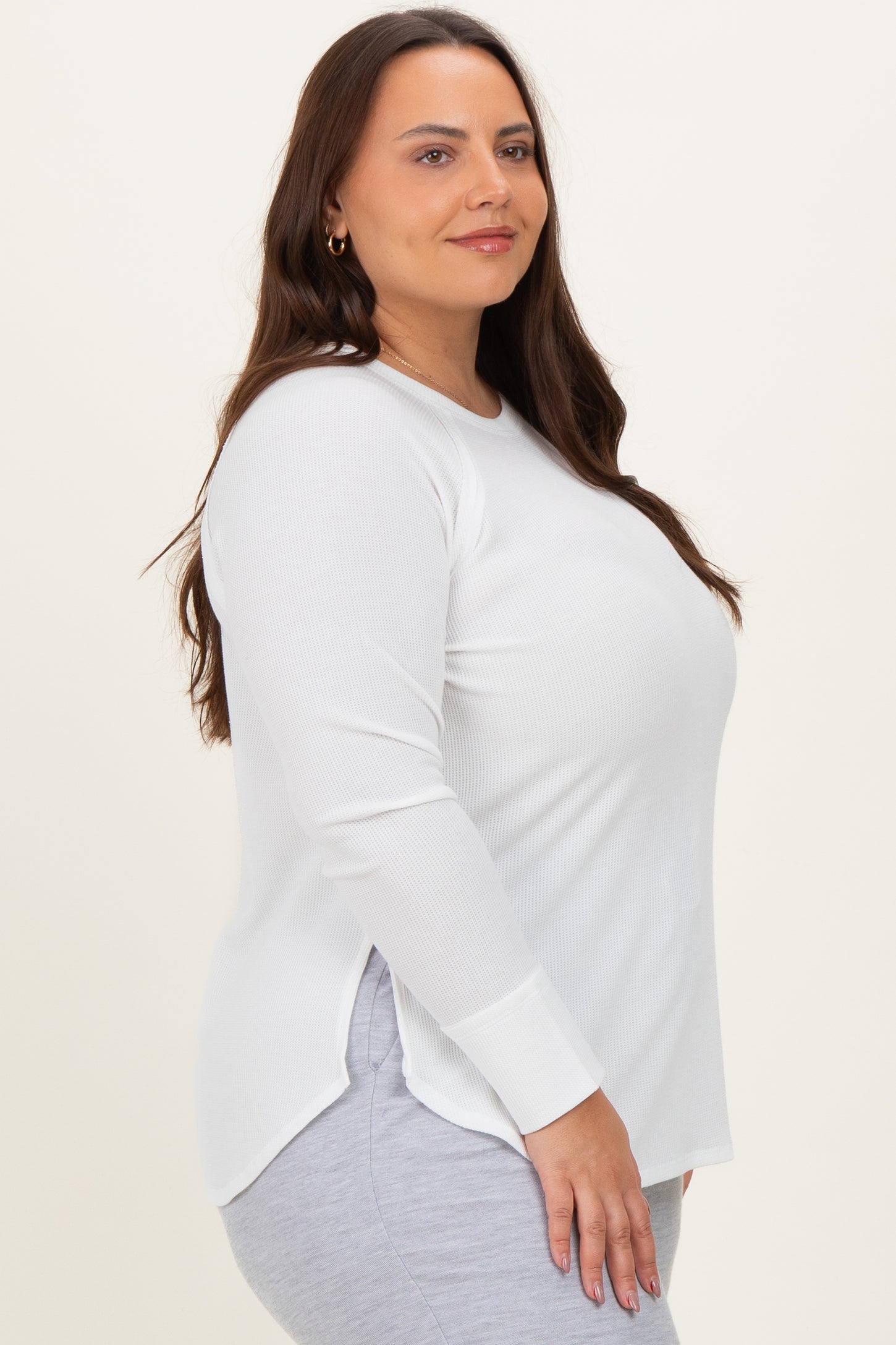 woman wearing a white long sleeve plus size top with side slits, styled with gray leggings