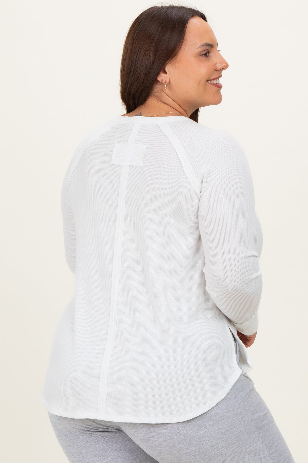 woman wearing a white long sleeve plus size top with a back detail, shown from the back