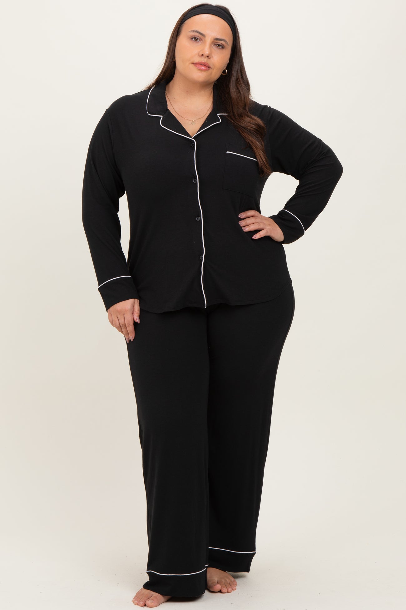 woman wearing a black plus size pajama set with white piping, includes long sleeve button-up top and matching pants