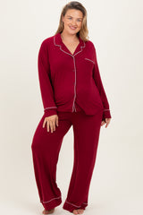 woman wearing a burgundy long sleeve maternity plus pajama set with white piping and smiling at the camera