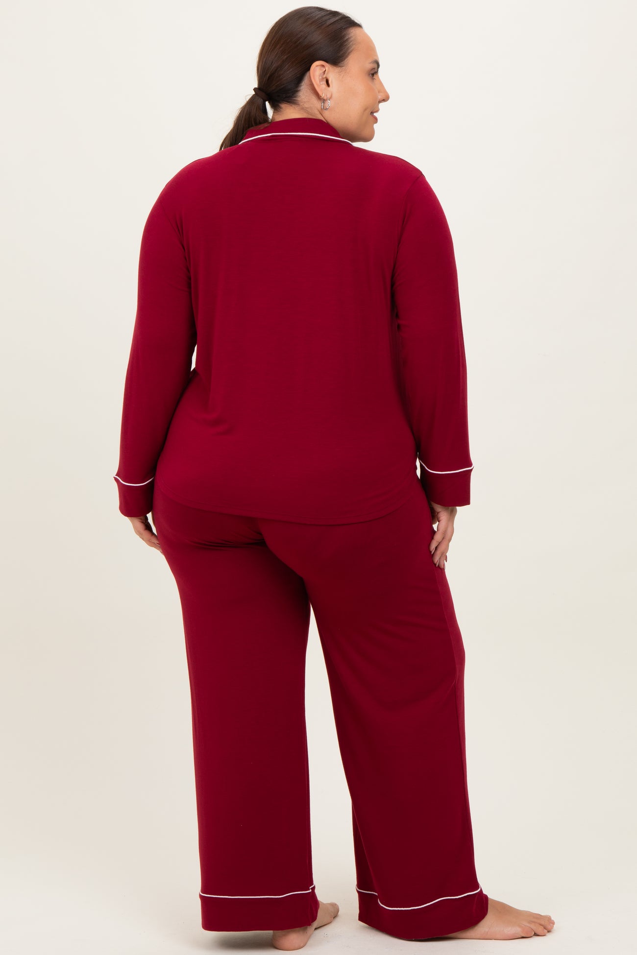 woman wearing a burgundy long sleeve pajama set with white piping, shown from the back