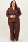 woman wearing a brown plus size pajama set with white piping and long sleeves, standing and smiling