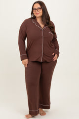 woman wearing a chocolate brown plus size pajama set with white piping and a pocket, standing barefoot on a light background