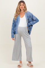 woman wearing a blue patterned maternity cardigan and grey wide-leg pants, showing her baby bump