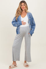 woman wearing a blue patterned maternity cardigan and gray wide-leg pants, holding her baby bump