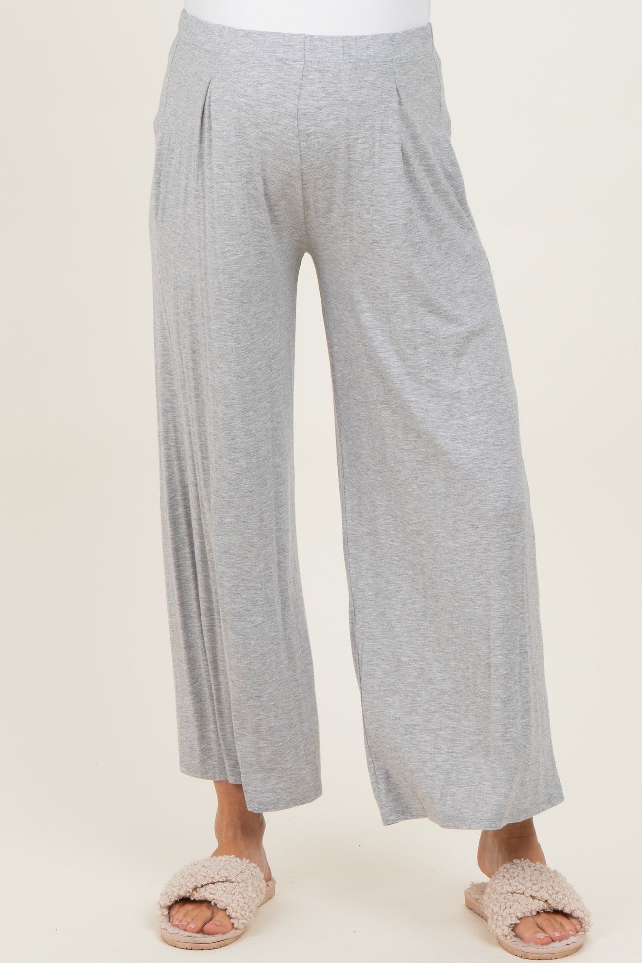 woman wearing light gray maternity wide leg pants with pleats, styled with cozy slippers