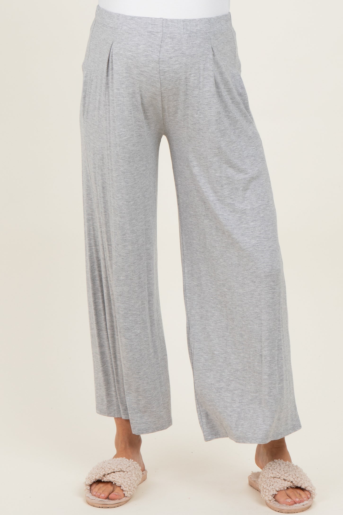 woman wearing light gray maternity wide leg pants with pleats, styled with cozy slippers