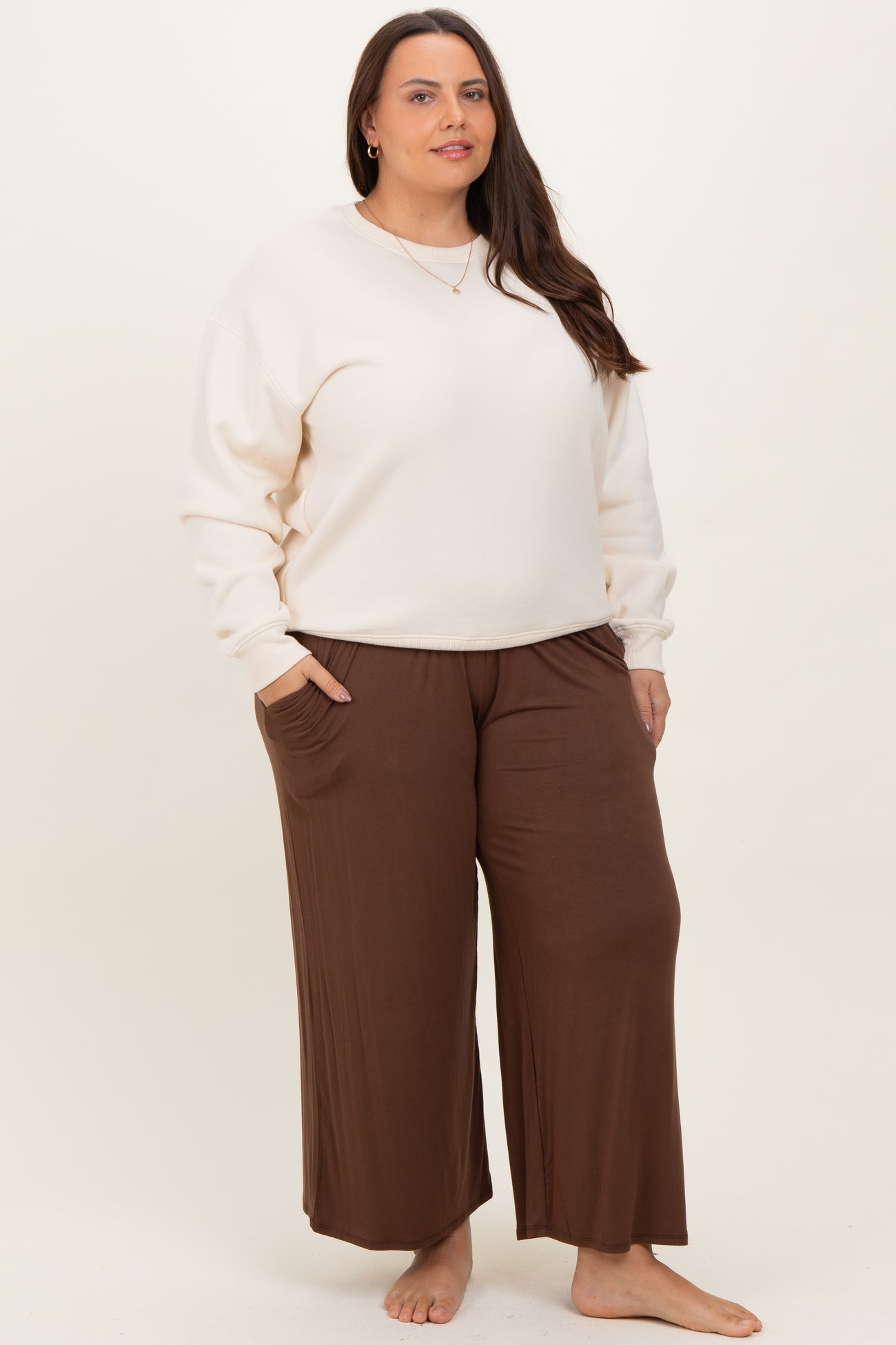 woman wearing a cream oversized sweatshirt and brown wide-leg pants, standing with hands in pockets