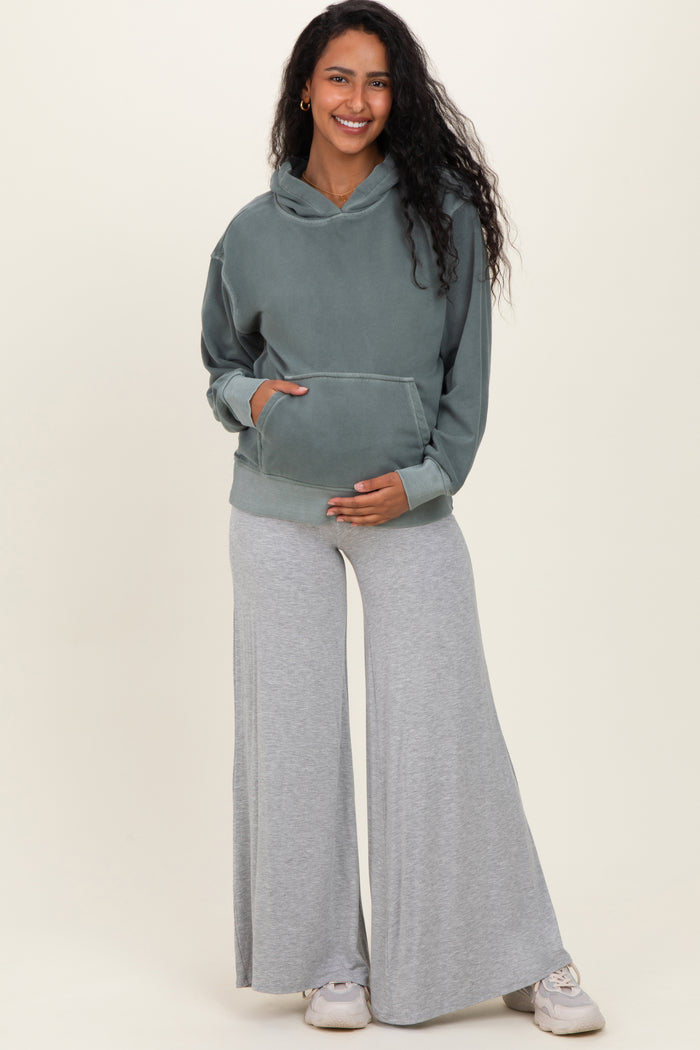 woman wearing a green maternity hoodie and gray wide-leg sweatpants, holding her baby bump