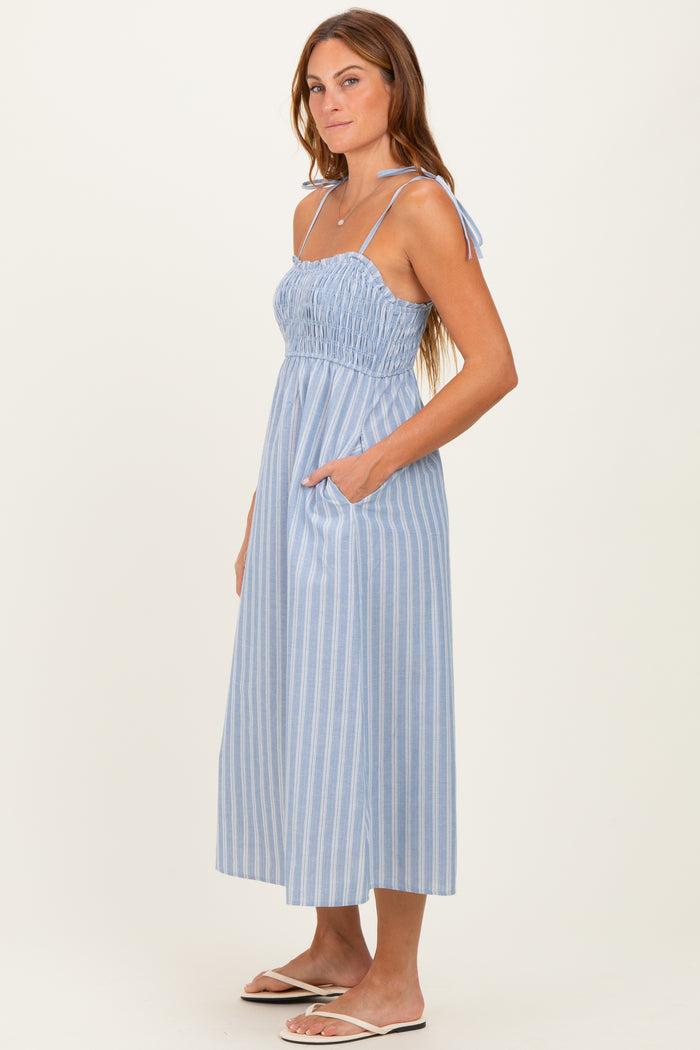 woman wearing a blue and white striped midi dress with a smocked bodice and tie straps, featuring side pockets