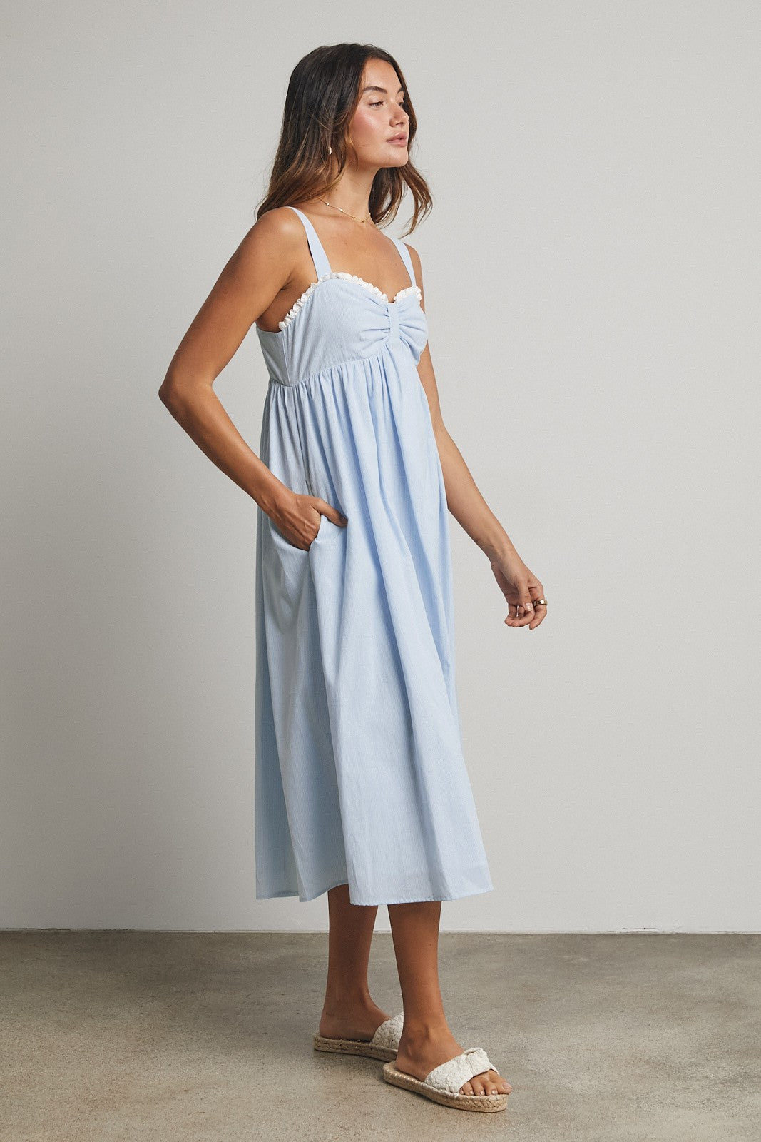 woman wearing a light blue midi dress with a gathered bodice and lace trim, featuring side pockets and wearing sandals
