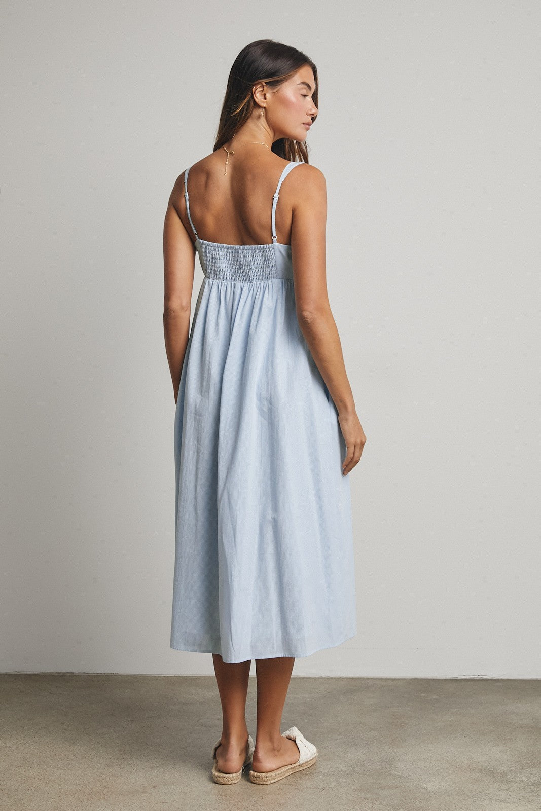woman wearing a light blue sleeveless midi dress with smocked back and standing backwards