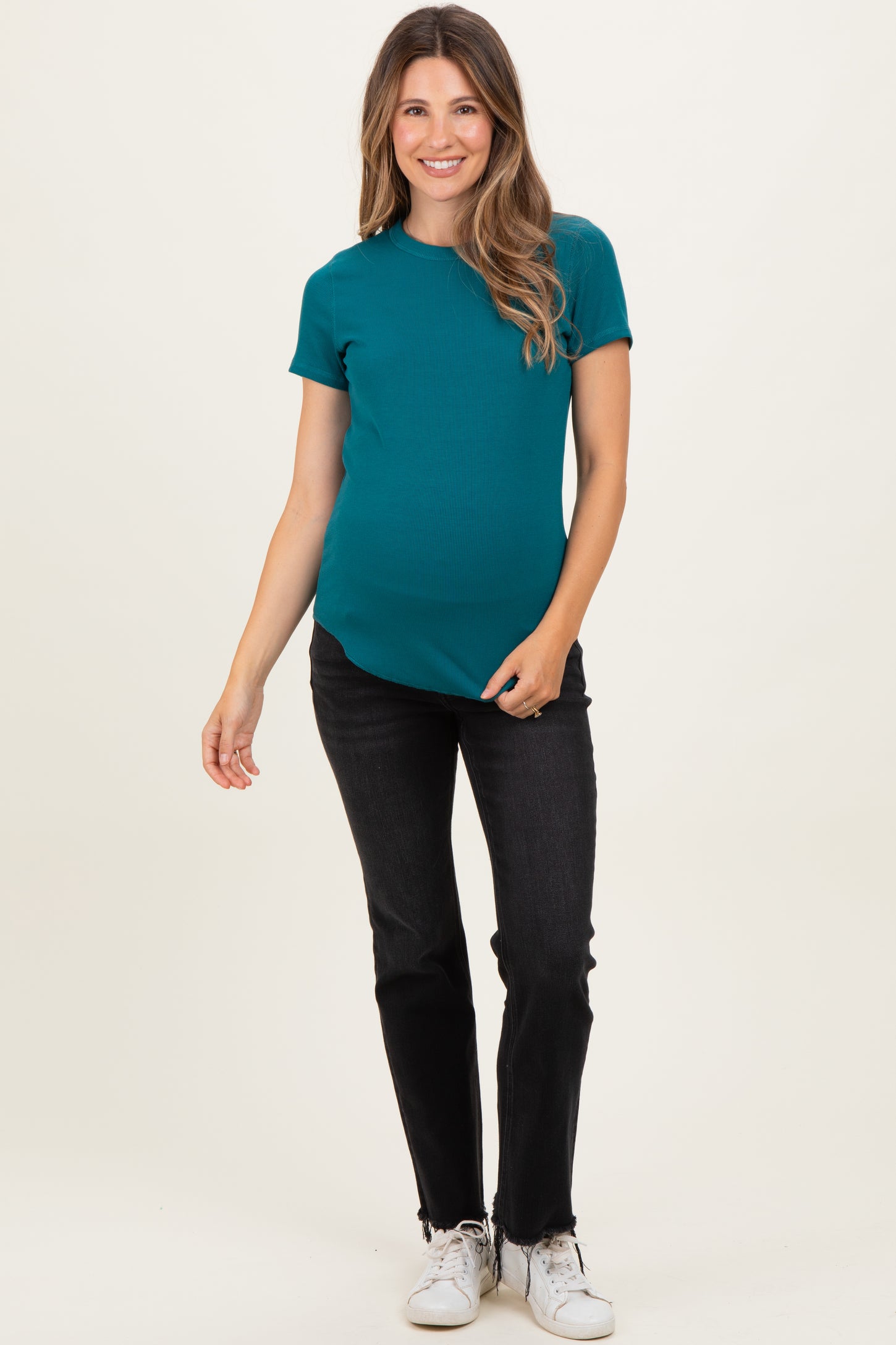 woman wearing a teal short sleeve maternity top and black jeans, showing her baby bump
