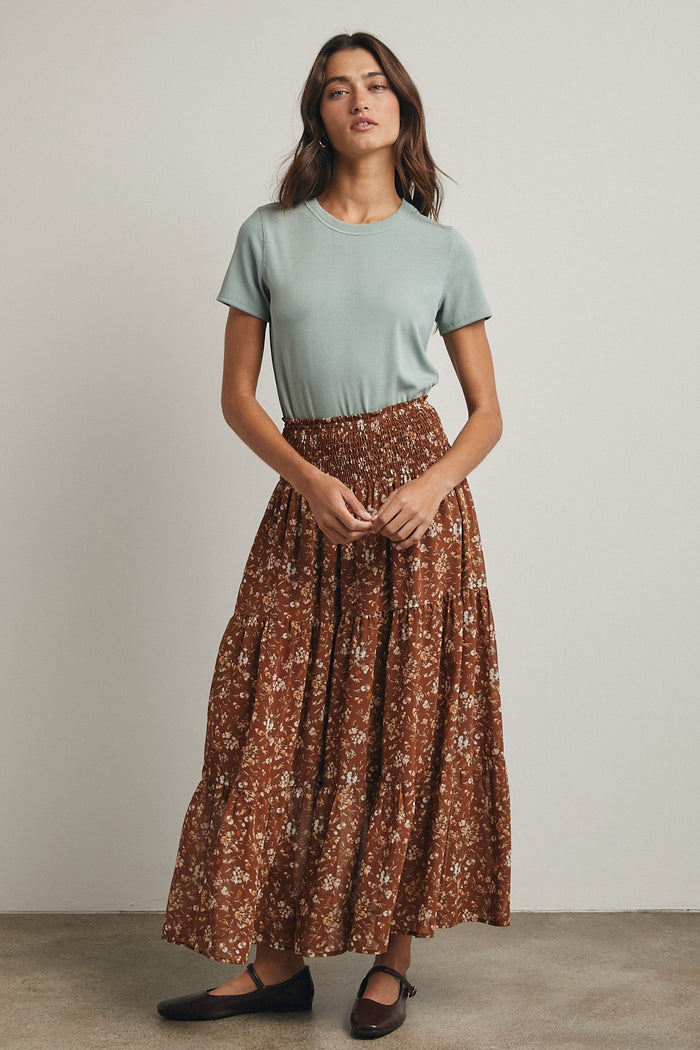 woman wearing a light green short sleeve top and a brown floral maxi skirt, styled casually