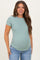 woman wearing a light green short sleeve maternity top and showing her baby bump while smiling