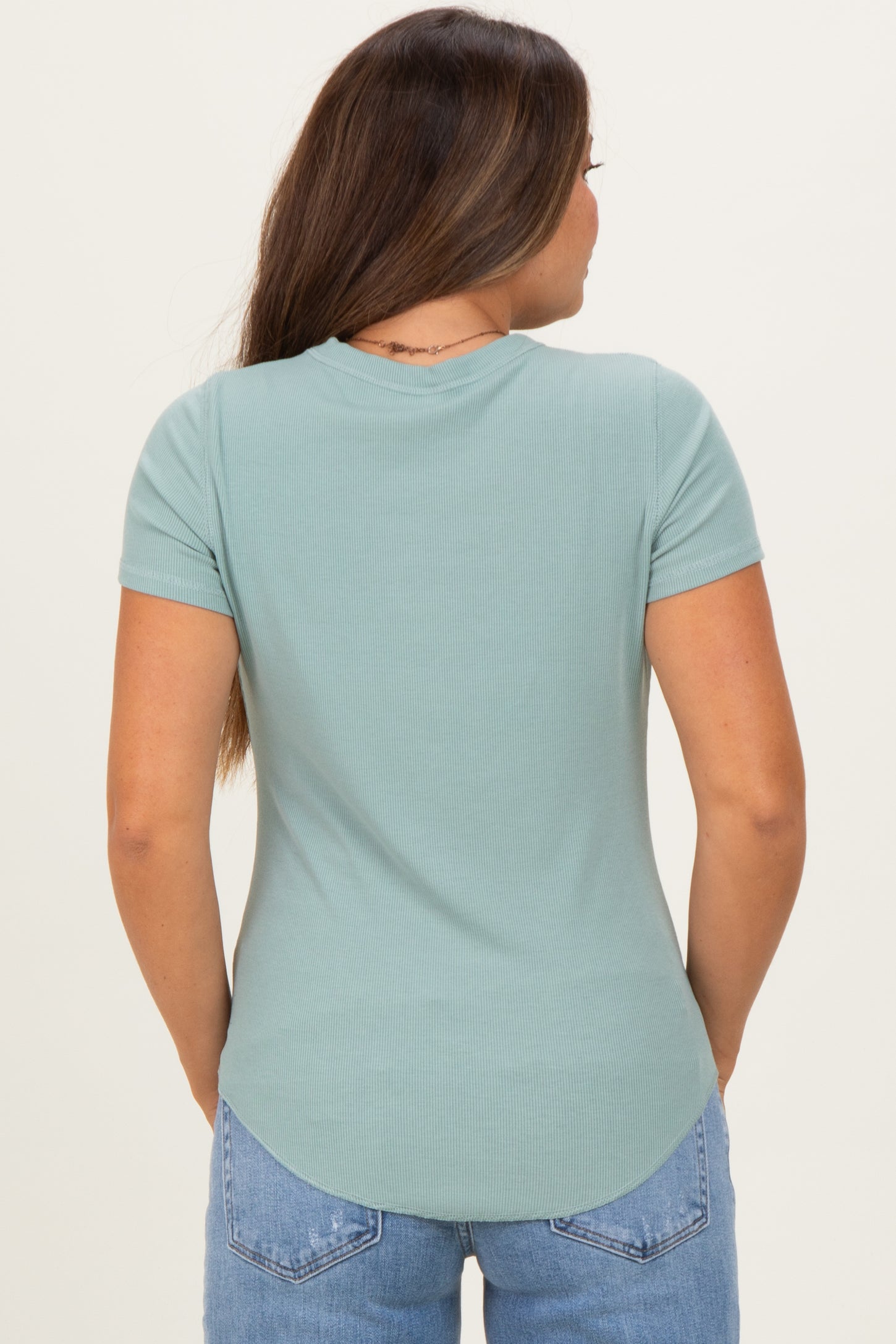 woman wearing a light green maternity top with short sleeves and a rounded hem, shown from the back