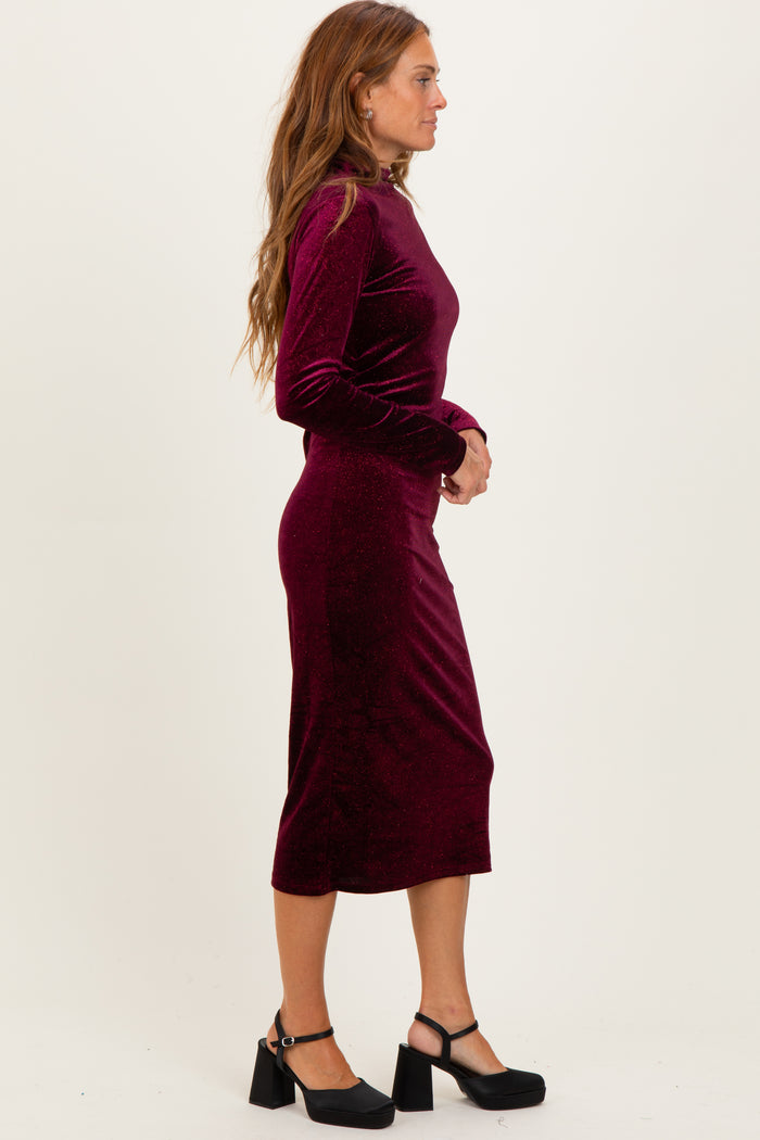 woman wearing a burgundy velvet long sleeve midi dress with a fitted silhouette and block heel shoes