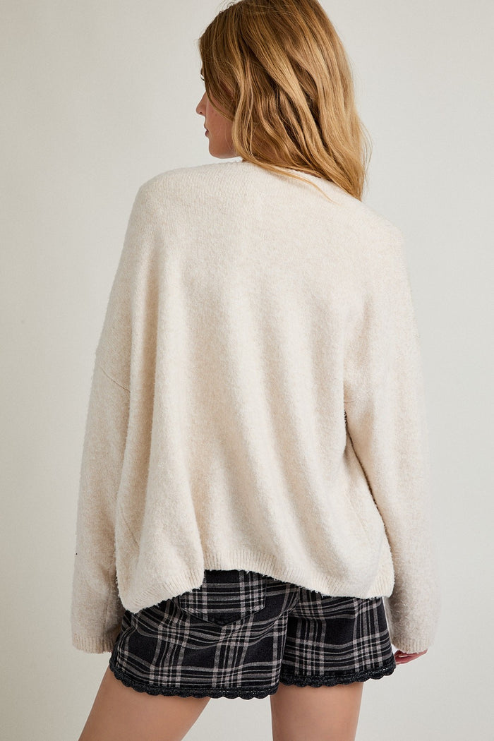 woman wearing a cozy cream oversized sweater paired with black and white plaid shorts, viewed from the back