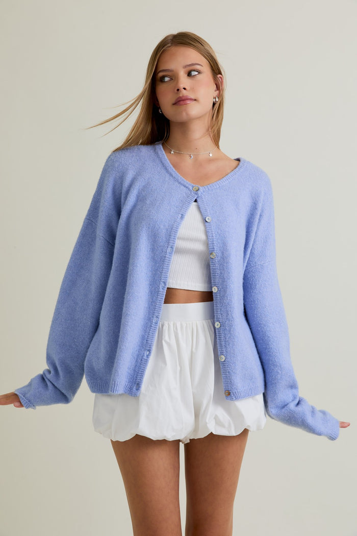 woman wearing a light blue oversized cardigan over a white cropped tank top and white skirt