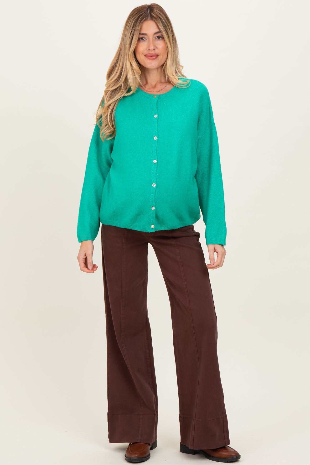 woman wearing a vibrant green maternity cardigan with buttons and brown wide-leg pants, showcasing her baby bump