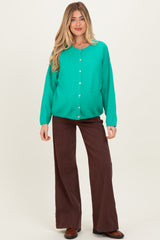 woman wearing a vibrant green maternity cardigan with buttons and brown wide-leg pants, showcasing her baby bump