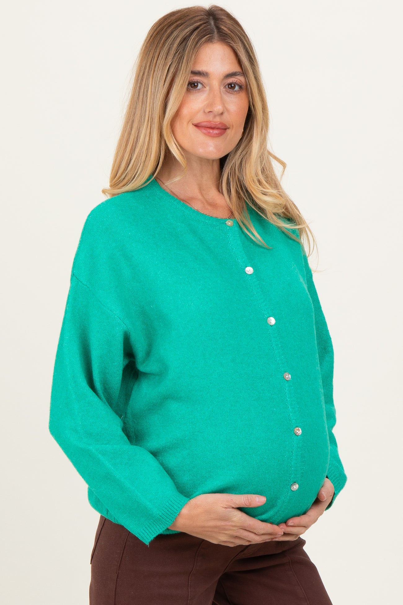 woman wearing a bright green maternity cardigan and holding her baby bump