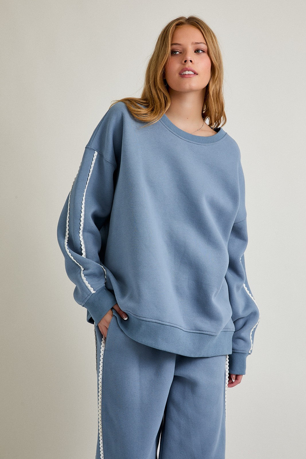 woman wearing a light blue oversized sweatshirt with lace trim details on the sleeves and matching bottoms