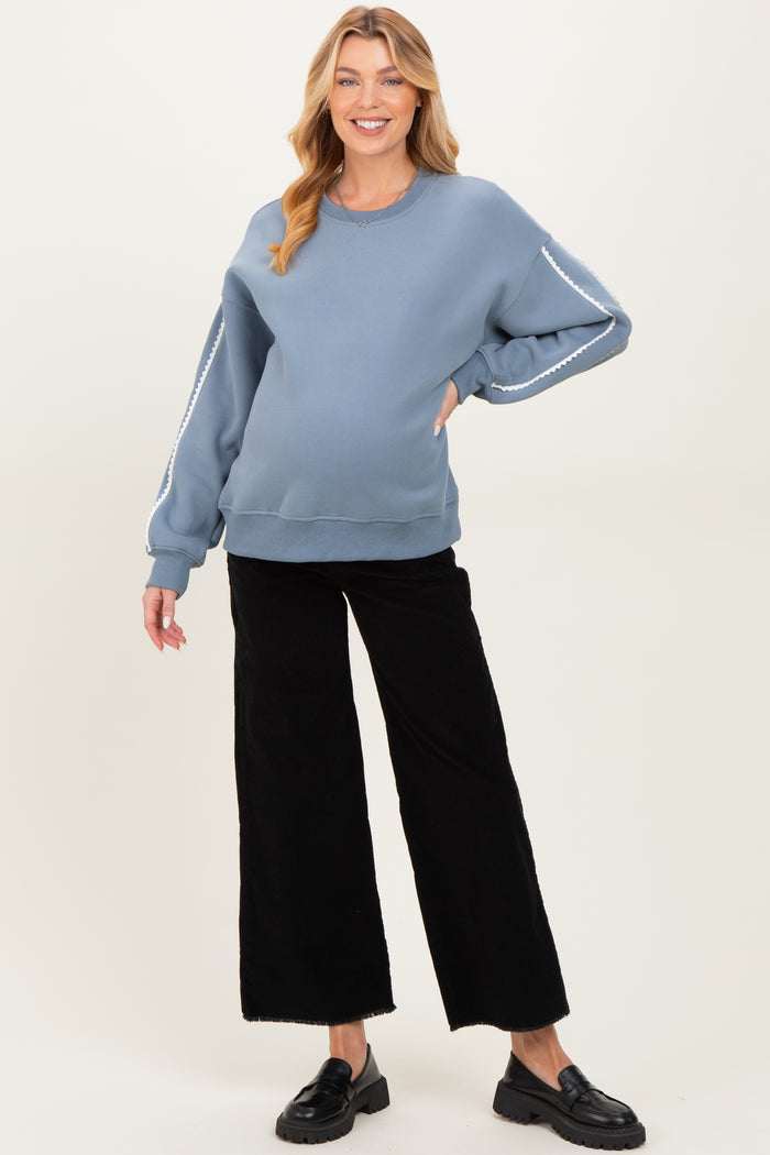 woman wearing a blue oversized maternity sweatshirt with decorative stripes on the sleeves and black wide-leg pants