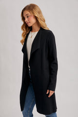 woman wearing a black long open-front coat over a white sweater and blue jeans