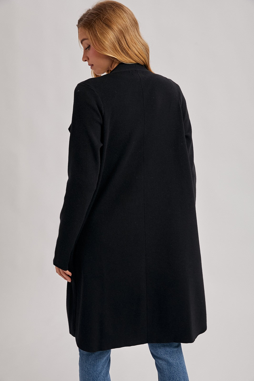 woman wearing a black long coat viewed from the back, paired with blue jeans