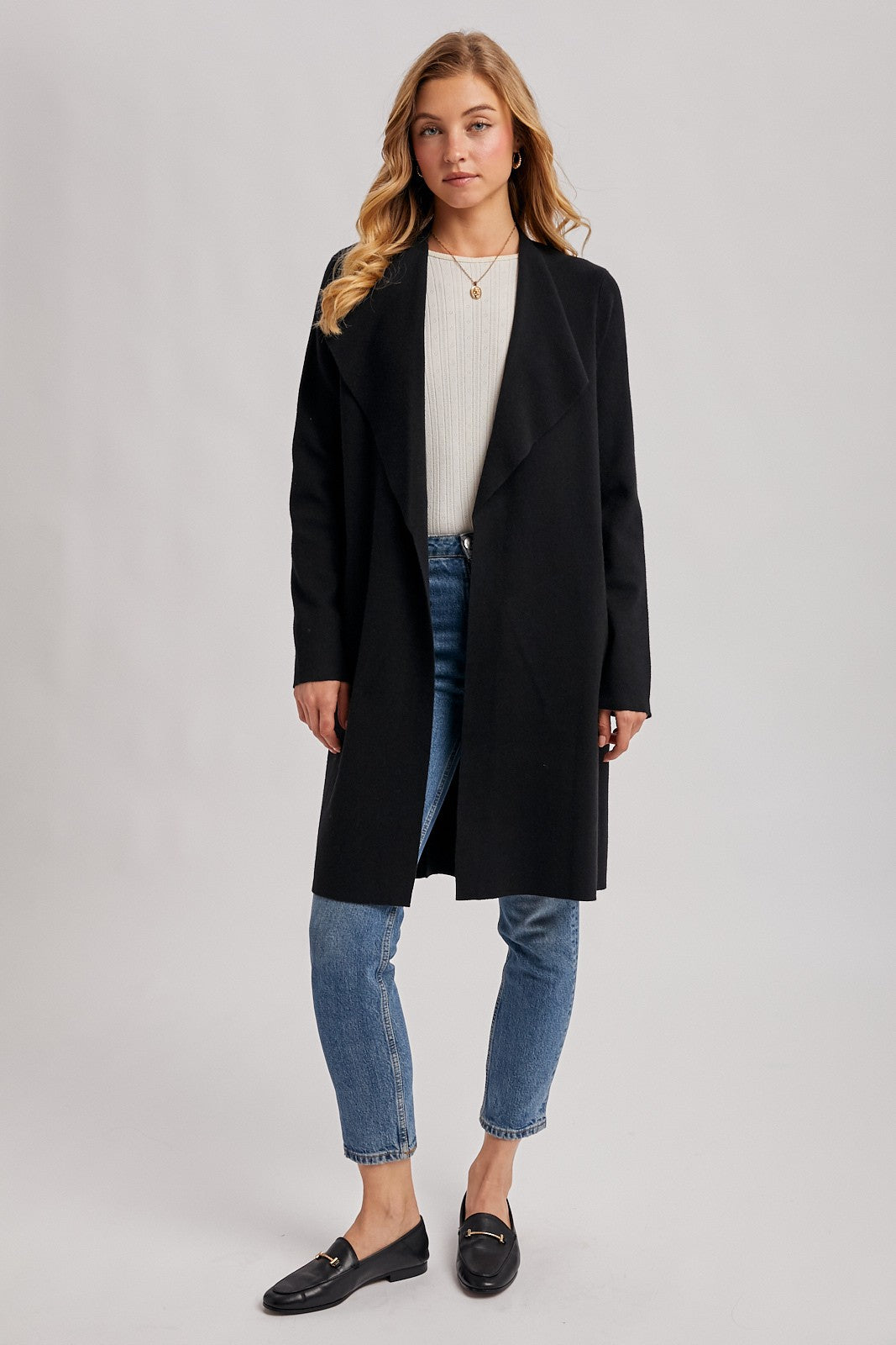 woman wearing a black long cardigan over a cream top, styled with blue jeans and black loafers