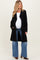 woman wearing a black open-front maternity coat over a white top and blue flared jeans, showing her baby bump