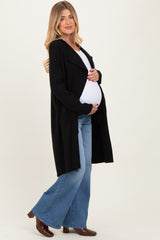 woman wearing a black long maternity cardigan and holding her baby bump while dressed in flared jeans and boots