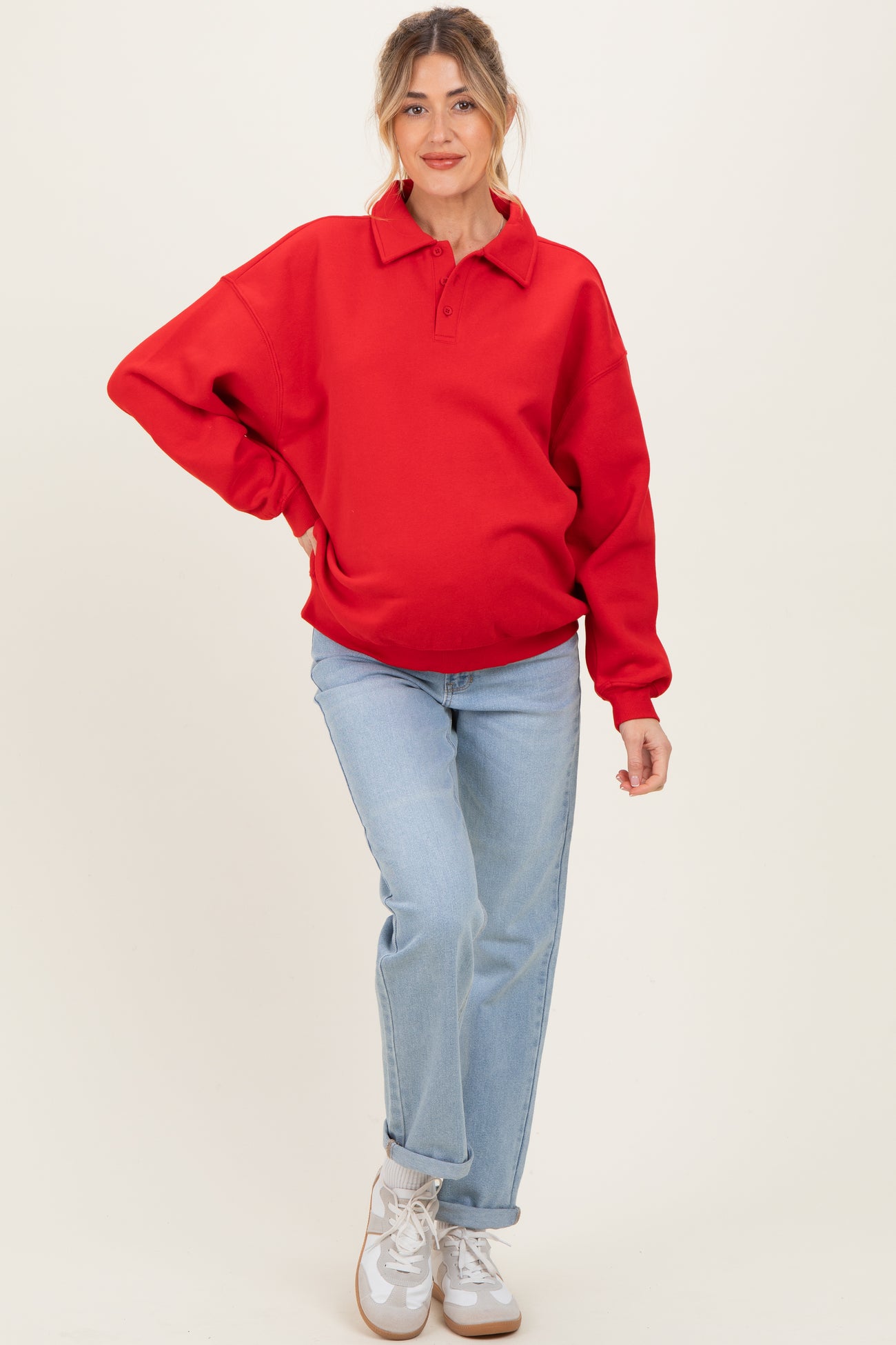 woman wearing a red oversized polo sweatshirt as maternity wear and blue straight-leg jeans, showing her baby bump