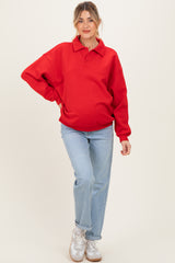 woman wearing a red oversized polo sweatshirt as maternity wear and blue straight-leg jeans, showing her baby bump
