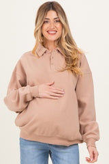 woman wearing a light brown maternity polo sweatshirt and holding her baby bump