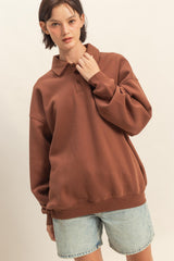 woman wearing a brown oversized polo sweatshirt with a collar and relaxed fit, paired with light blue denim shorts