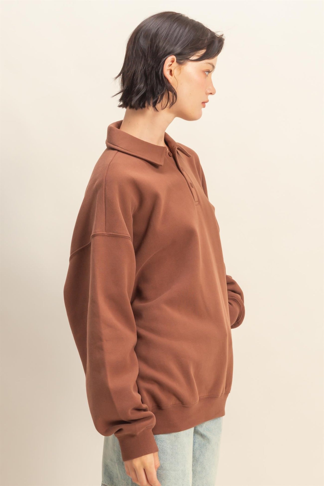 woman wearing a brown oversized polo sweatshirt with a collar and side pockets