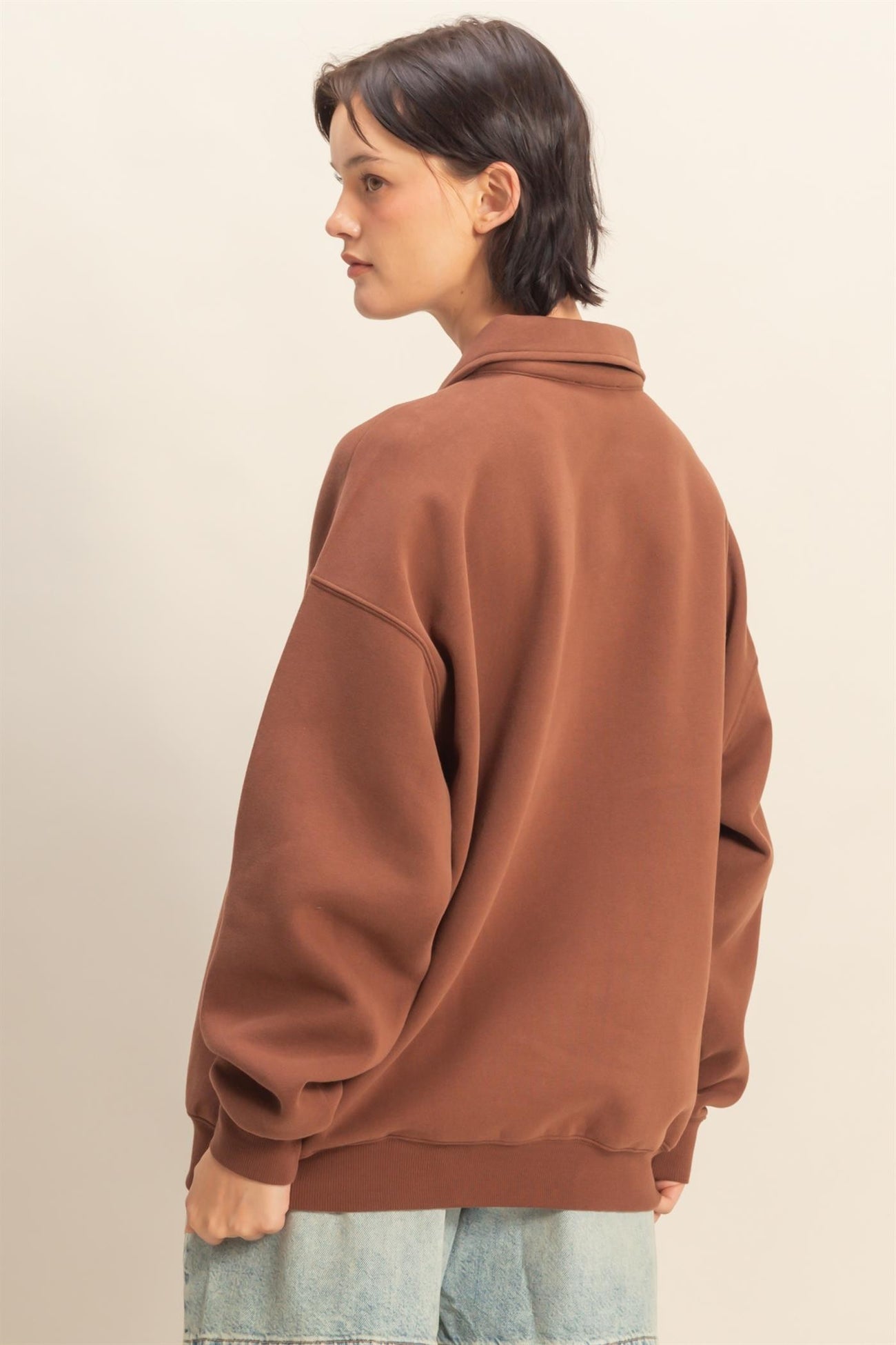woman wearing a brown oversized sweatshirt with a collar, showing the back view and relaxed fit