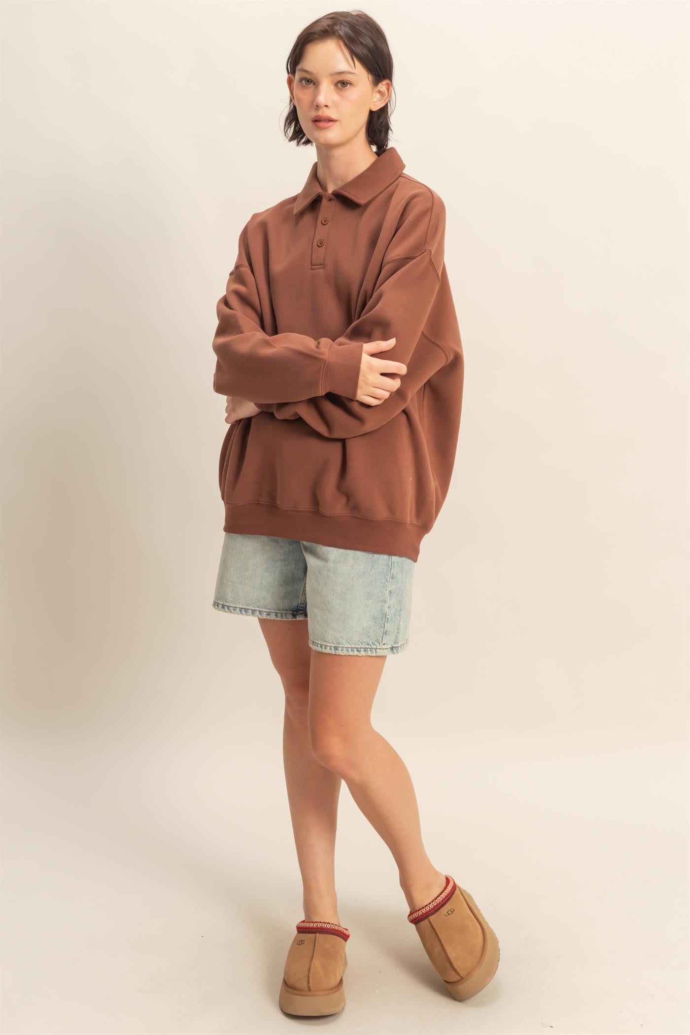 woman wearing a brown oversized polo sweatshirt with denim shorts and tan moccasin slippers
