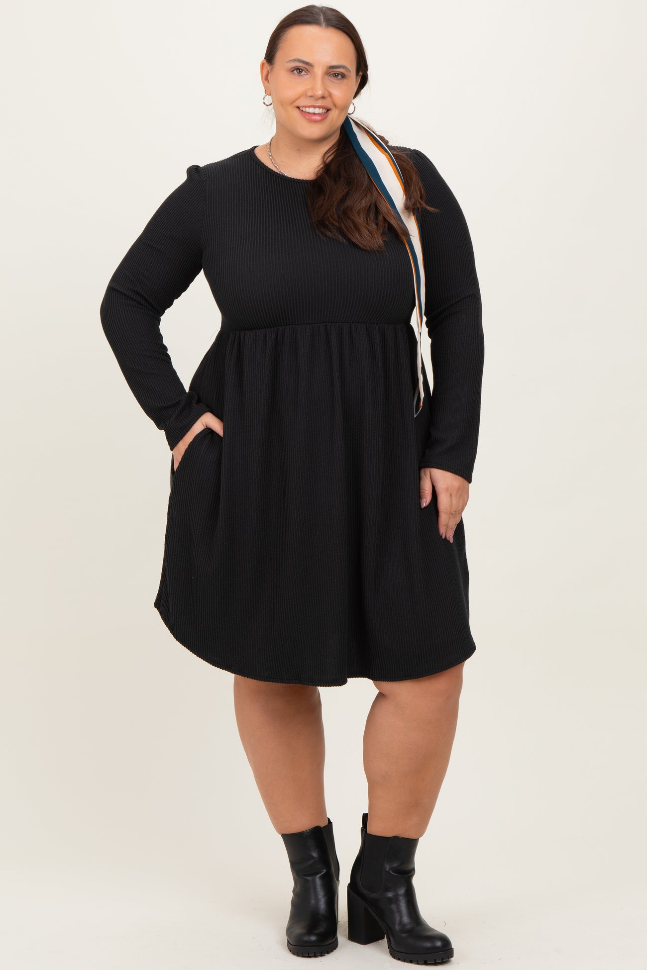 woman wearing a black long sleeve plus size dress with a flared skirt and pockets, styled with ankle boots