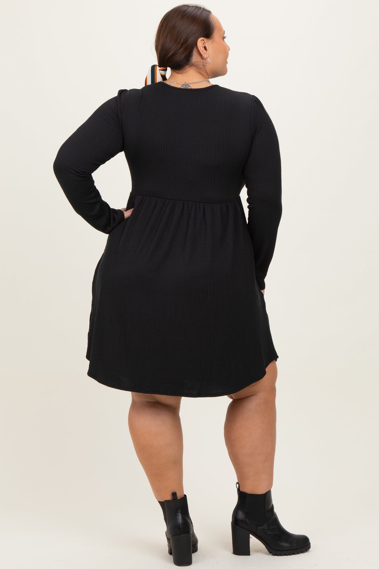 woman wearing a black long sleeve plus size dress with a flared skirt and ankle boots, viewed from the back