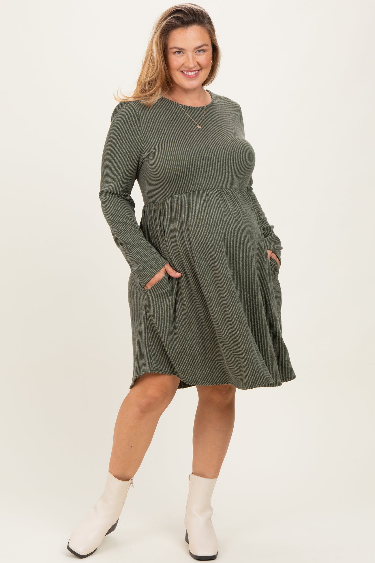 woman wearing an olive green long sleeve maternity dress with pockets and a visible baby bump