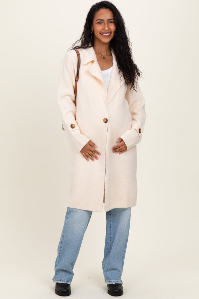 woman wearing a light cream maternity coat with buttons and paired with blue jeans