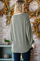 woman wearing a green oversized knit sweater with white trim, viewed from the back against a brick wall