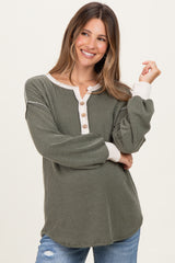 woman wearing a green ribbed maternity top with a button detail and cream-colored cuffs, smiling and holding her baby bump