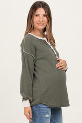 woman wearing a green maternity sweater with buttons and long sleeves, gently cradling her baby bump