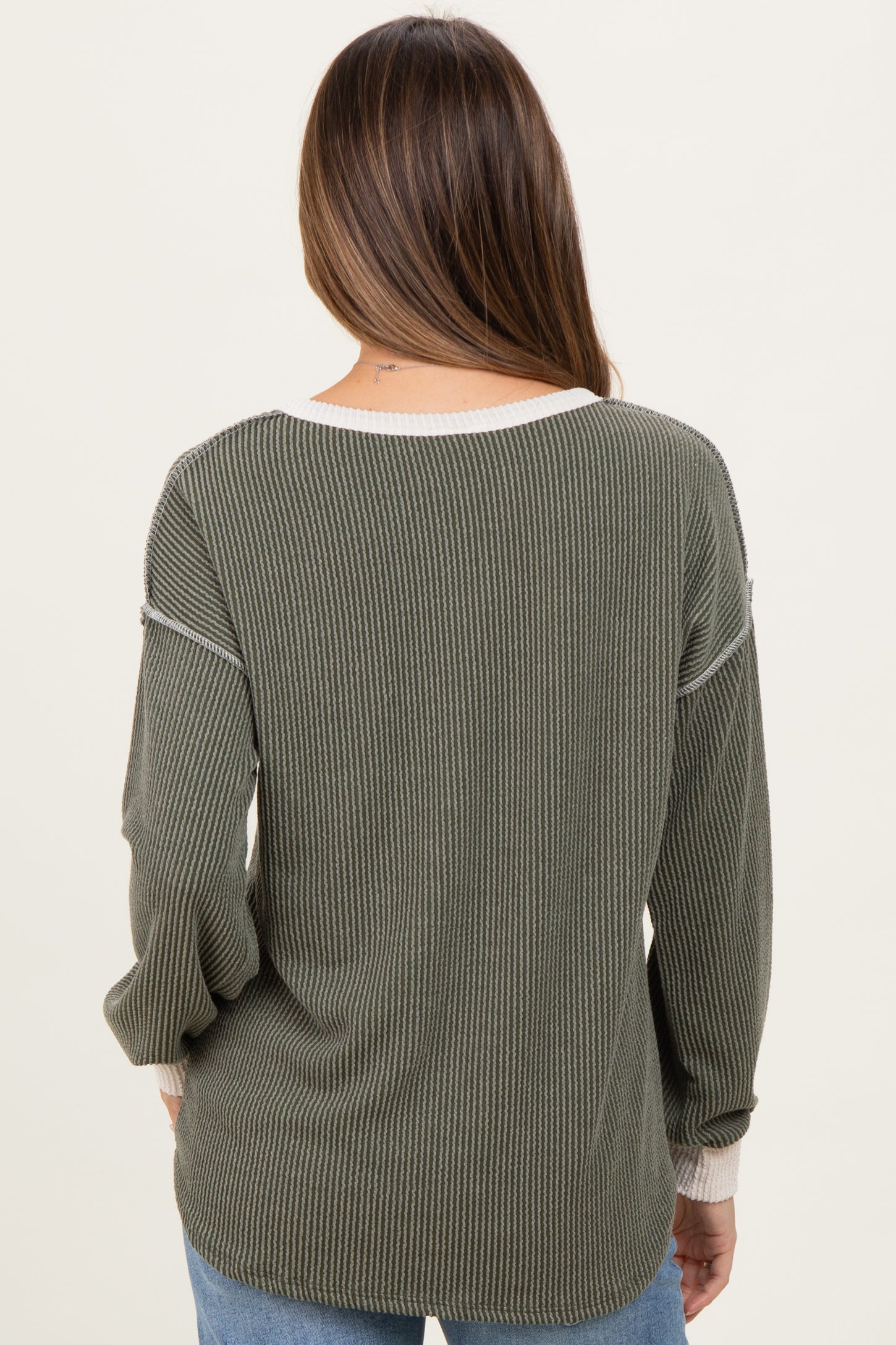 woman wearing a dark green maternity sweater with ribbed texture and light cream accents, showing her back